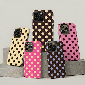 May include: A collection of phone cases with a polka dot pattern. The cases are in various colors, including brown, pink, and yellow. The polka dots are in contrasting colors. The cases are displayed on a gray surface.