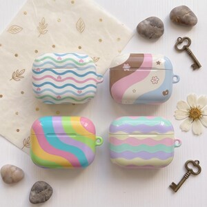 May include: Four rectangular protective cases for wireless earbuds, each featuring distinct patterns. One has blue wavy lines with small hearts, another has brown, pink, and blue swirls with flowers, one has rainbow-colored waves, and one has pastel wavy stripes.