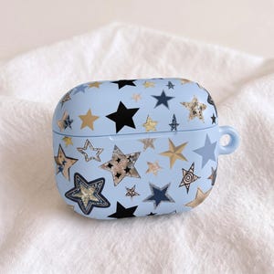 Pode incluir: Uma capa protetora azul-clara para auriculares sem fios com um padr&atilde;o disperso de estrelas de v&aacute;rios tamanhos, cores e texturas, incluindo preto s&oacute;lido, azul-marinho, dourado met&aacute;lico, glitter prateado e desenhos de estrelas contornadas.