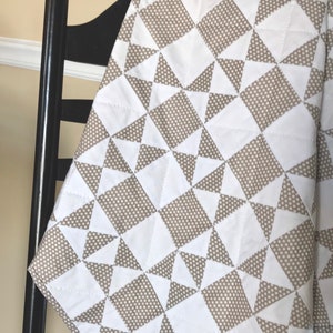 K&ouml;nnte beinhalten: Eine wei&szlig;e und braune Steppdecke mit geometrischem Muster. Die Steppdecke ist aus Baumwollstoff und f&uuml;hlt sich weich und angenehm an.