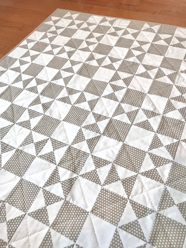 K&ouml;nnte beinhalten: Eine wei&szlig;e und graue Steppdecke mit einem geometrischen Muster aus Quadraten und Dreiecken. Die Steppdecke besteht aus zwei Stoffen, einem mit wei&szlig;em Hintergrund und dem anderen mit grauem Hintergrund mit wei&szlig;en Punkten.