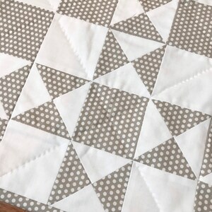 K&ouml;nnte beinhalten: Eine Steppdecke aus wei&szlig;em und braunem Stoff mit einem Tupfenmuster. Die Steppdecke besteht aus Quadraten und Dreiecken.