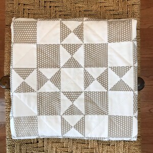 K&ouml;nnte beinhalten: Eine wei&szlig;e und graue Steppdecke mit einem geometrischen Muster aus Quadraten und Dreiecken. Die Steppdecke besteht aus zwei Stoffen, einem mit wei&szlig;em Hintergrund und grauen Punkten und einem mit grauem Hintergrund und wei&szlig;en Punkten.