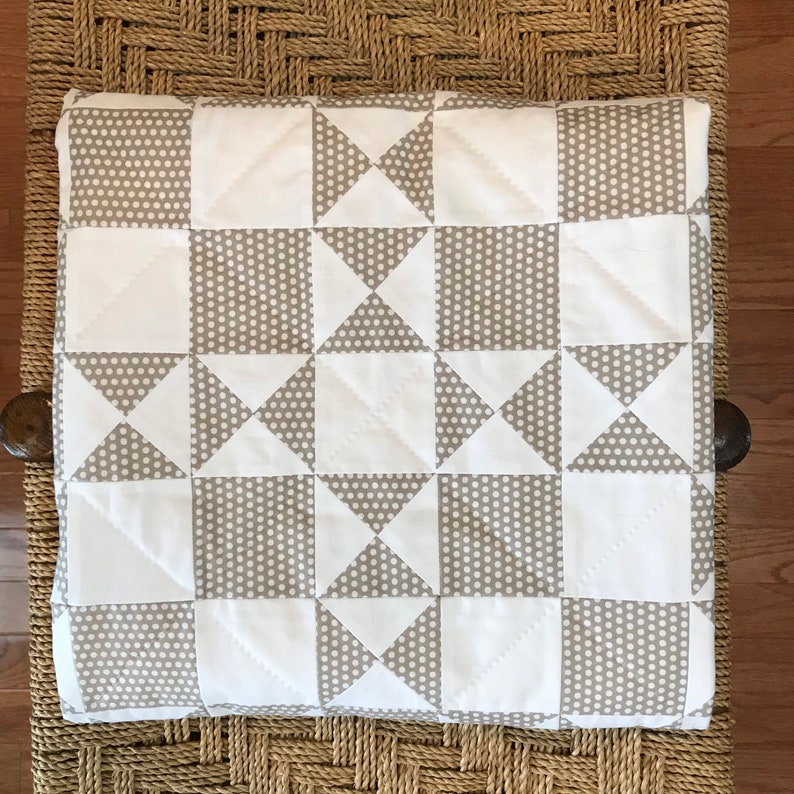 K&ouml;nnte beinhalten: Eine wei&szlig;e und graue Steppdecke mit einem geometrischen Muster aus Quadraten und Dreiecken. Die Steppdecke besteht aus zwei Stoffen, einem mit wei&szlig;em Hintergrund und grauen Punkten und einem mit grauem Hintergrund und wei&szlig;en Punkten.