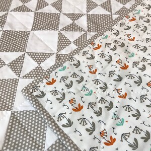 K&ouml;nnte beinhalten: Eine graue und wei&szlig;e Steppdecke mit einem geometrischen Muster auf der einen Seite und einem wei&szlig;en Stoff mit einem Blumenmuster auf der anderen Seite.