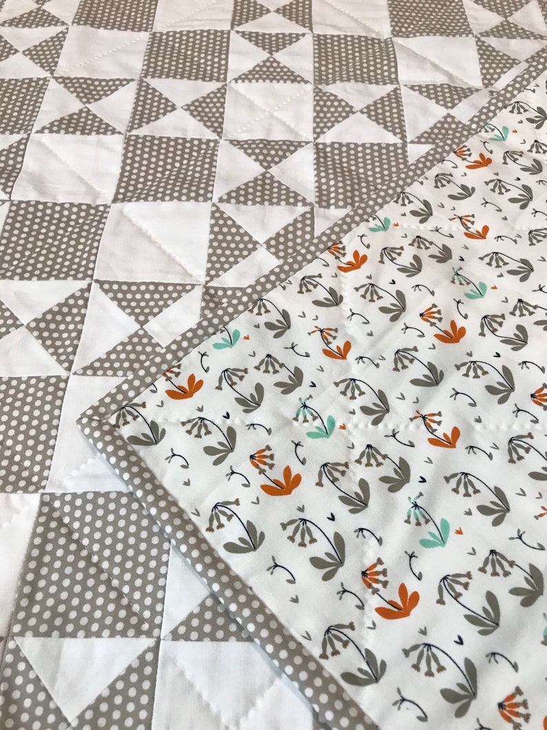 K&ouml;nnte beinhalten: Eine graue und wei&szlig;e Steppdecke mit einem geometrischen Muster auf der einen Seite und einem wei&szlig;en Stoff mit einem Blumenmuster auf der anderen Seite.