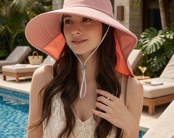 May include: A pale pink sun hat with a wide brim and a chin strap. The hat has an orange lining and is designed for sun protection. The hat is worn by a person near a swimming pool.