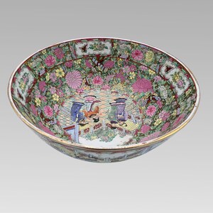 Peut inclure: Un grand bol rond en porcelaine avec un motif floral et figuratif détaillé. Le bol présente un bord doré et est rempli de fleurs roses, jaunes et vertes. L'intérieur représente des personnages dans un cadre de cour.