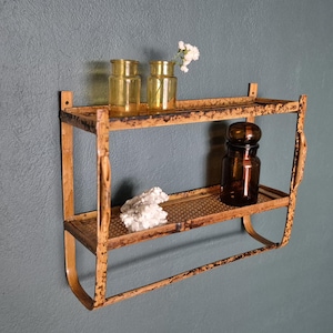 May include: An antique, two-tiered metal shelf with a distressed, orange finish. The shelf holds two yellow glass bottles, a brown glass jar, and a piece of white stone. The shelf is mounted on a gray wall.