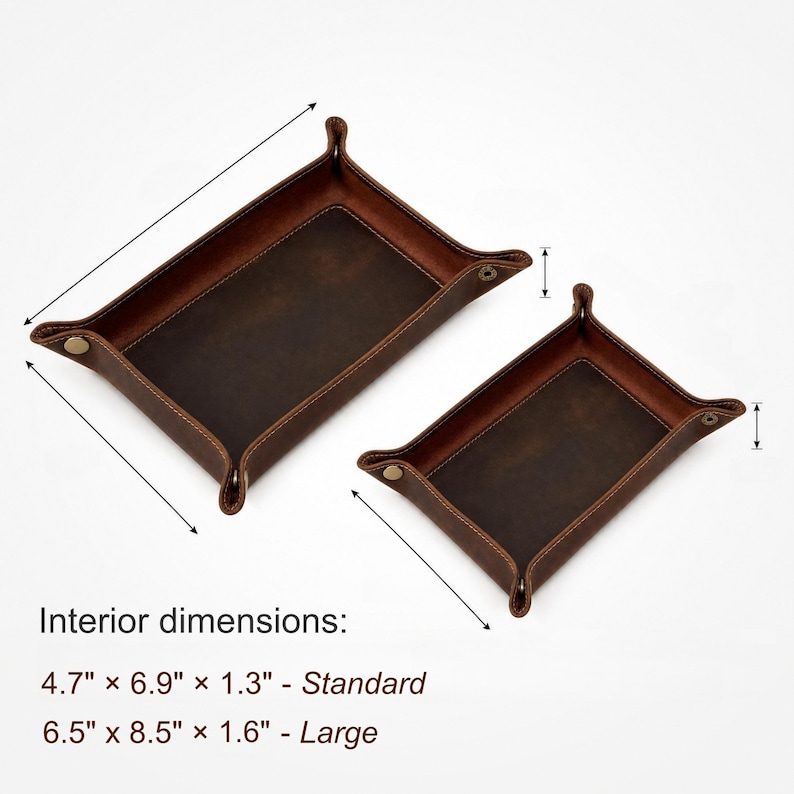 May include: Two brown leather catchall trays with snap closures. The larger tray measures 6.5" x 8.5" x 1.6", and the smaller tray is 4.7" x 6.9" x 1.3". The trays have a rectangular shape with raised edges and are designed to hold small items.