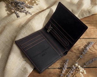 May include: Open brown leather wallet with a zipper pocket and multiple card slots. The interior is black with the inscription "To infinity, and beyond." and initials. The wallet is on a wooden surface with lavender sprigs.