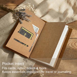 May include: A brown kraft paper pocket insert for a notebook featuring two horizontal slots for cards or notes. The insert is open, revealing white lined pages inside. Text on the image reads: Pocket Insert, Fits cards, notes, tickets & more, Keeps essentials organized for travel or journaling.