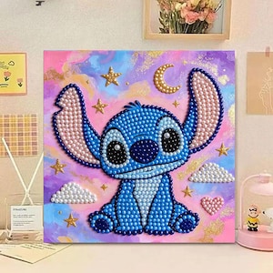 May include: A square diamond painting art piece featuring a blue alien character with large ears, surrounded by gold glitter stars, a crescent moon, white pearl clouds, and a pink heart, all set against a vibrant purple, pink, and blue painted background.