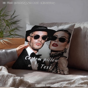 May include: A square pillow with a printed image of a man and woman wearing sunglasses. The pillow has the text "Custom pillow with Text" printed on it. The pillow is on a gray couch.