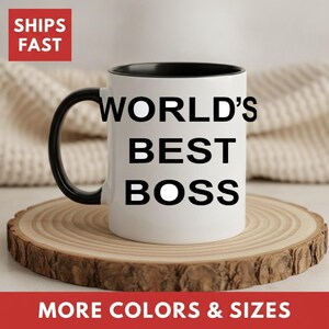 May include: A white ceramic mug with a black handle and interior. The exterior features the black text "WORLD'S BEST BOSS" printed in a bold, sans-serif font. The mug has a cylindrical body and a curved handle on the left side of the design.