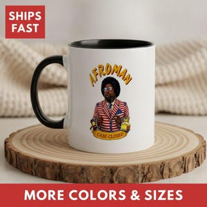 May include: A white ceramic mug with a black handle and interior. The front features a graphic of a person with an afro wearing a red, white, and blue striped suit and sunglasses, holding a gavel. The text reads AFROMAN and CASE CLOSED.