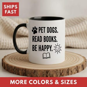 May include: A white ceramic mug with a black handle and interior. The mug features black text that reads PET DOGS. READ BOOKS. BE HAPPY. accompanied by a black paw print icon, an open book icon, and a smiling sun icon printed on the front.