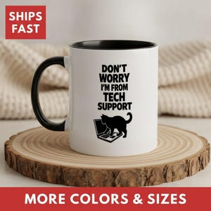 May include: A white ceramic mug with a black interior and handle. The front features black text that reads "DON'T WORRY I'M FROM TECH SUPPORT" above a black silhouette graphic of a cat sitting at a laptop computer, facing toward the right.