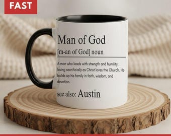 May include: A white ceramic mug with a black handle and interior. The mug features black printed text that reads: Man of God [m-an of God] noun. A man who leads with strength and humility, loving sacrificially as Christ loves the Church. He builds up his family in faith, wisdom, and devotion. see also: Austin.