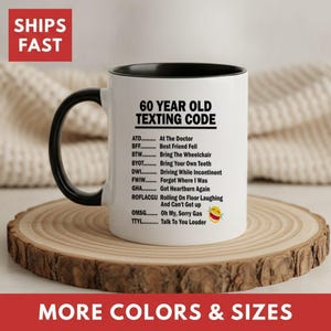 May include: A white ceramic mug with a black handle and interior, featuring the black printed text 60 YEAR OLD TEXTING CODE followed by a list of humorous acronym definitions and a laughing emoji with tears, all in a clear sans-serif font.