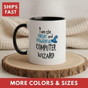 May include: A white ceramic mug with a black handle and interior rim. The mug features black and blue text that reads I am the GREAT and POWERFUL COMPUTER WIZARD, accompanied by a small blue wizard hat graphic with white star accents.
