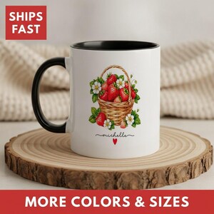 May include: A white ceramic mug with a black handle and interior rim. The front features a graphic of a woven basket filled with red strawberries and green leaves. Below the basket, the name Michelle is printed in black script with a red heart.