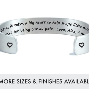 May include: Silver cuff bracelet with a personalized inscription that reads "It takes a big heart to help shape little minds. Thanks for being our au pair. Love, Alex, Ann" and two small heart symbols.