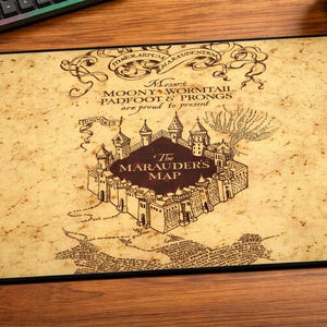 May include: A rectangular mousepad featuring a vintage-style map design. The map is in shades of brown and beige, with the text "The Marauders Map" prominently displayed. Additional text includes "Messrs Moony, Wormtail, Padfoot & Prongs are proud to present."