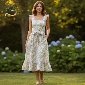 May include: A cream-colored floral print dress with blue flowers. The dress has a square neckline, ruffled straps, a tie-waist, and a ruffled hem. The dress is knee-length and has pockets. The woman is wearing sandals.