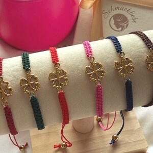 May include: Six colourful friendship bracelets with gold-coloured four-leaf clover charms. The bracelets are red, green, pink, navy blue, and brown. Each bracelet has a sliding knot closure for adjustable sizing.