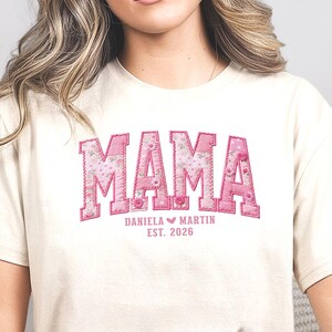 Peut inclure: T-shirt crème avec le mot "MAMA" en rose, lettres en blocs à motifs floraux. En dessous, le texte "DANIELA MARTIN EST. 2026". Le mot "NATURAL" est imprimé en bas de l'image.