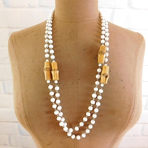Puede incluir: Un collar de doble cadena hecho de cuentas blancas con separadores de bambú natural. El collar se muestra en un maniquí marrón.