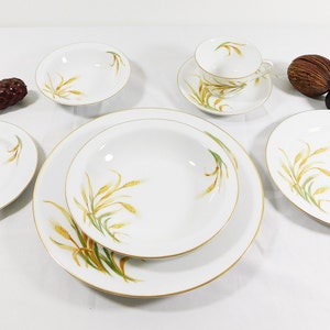 May include: A white porcelain dinnerware set with a wheat stalk design in gold and green. The set includes plates, bowls, and a teacup with saucer. The rims are trimmed with gold. A classic and elegant tableware collection.