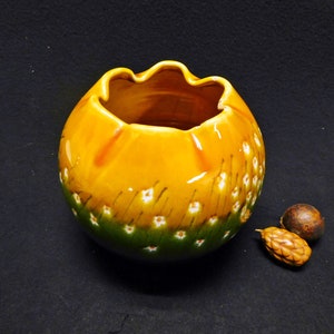 以下が含まれることがあります： 白の花柄が施された黄色と緑の陶器の花瓶。花瓶は広く丸い開口部と質感のある表面をしています。