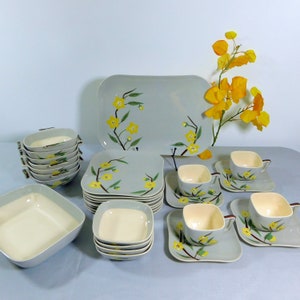 Puede incluir: Un juego de vajilla de cerámica gris y blanca con un patrón floral con flores amarillas y hojas verdes. El juego incluye una bandeja grande para servir, platos cuadrados, tazones y tazas de té con platillos.