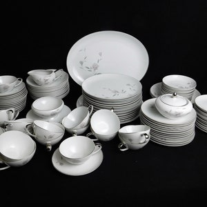 Pode incluir: Um conjunto de louça de porcelana branca com um delicado desenho floral. O conjunto inclui pratos, tigelas, chávenas e pires.