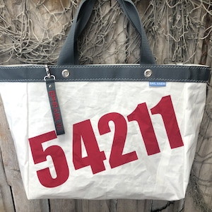 May include: White canvas tote bag with a red number "54211" printed on the front. The bag has a gray top and a small blue tag that says "Sail Away".