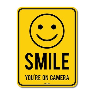 May include: Yellow rectangular sign with a black border. The sign features a black smiley face at the top, the word "SMILE" in bold black letters, and the text "YOU'RE ON CAMERA" below. The sign also has the text "SG186" at the bottom.