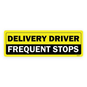 May include: A rectangular yellow sign with black text that reads "DELIVERY DRIVER" above "FREQUENT STOPS" in white. The sign has a black border and a small code in the bottom right corner.