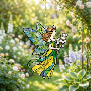 Puede incluir: Atrapasoles de hada de vidriera con alas verdes y azules, vestida con un vestido amarillo y verde. Sostiene un ramo de flores blancas. Colgando de una cadena plateada.