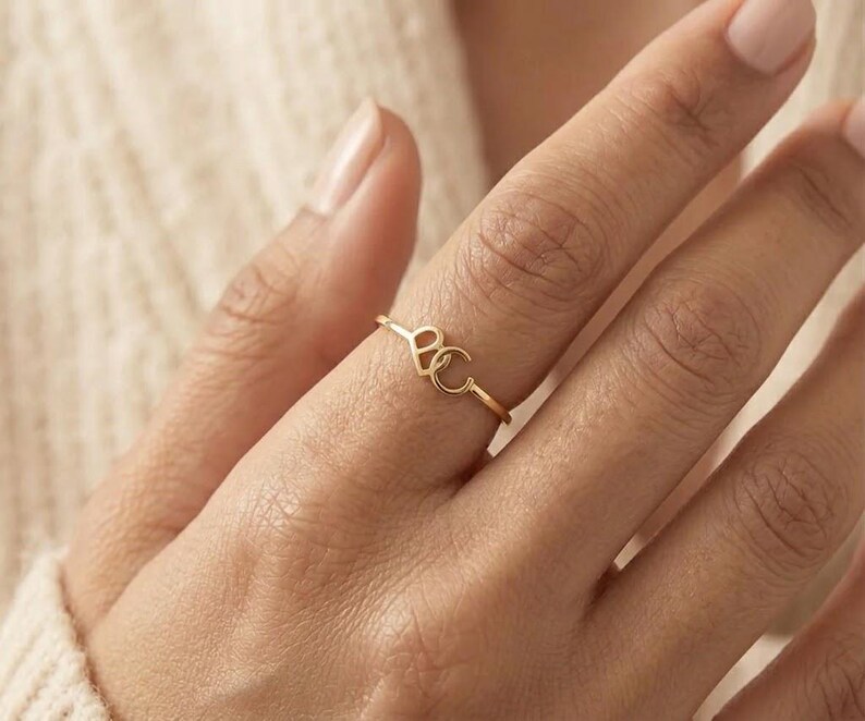 May include: A thin gold ring featuring a small heart-shaped charm and a letter C charm attached to the band. The metal has a polished finish, and the two charms are positioned side-by-side on the top of the ring, creating a delicate and simple design.
Custom Cursive Initial Ring, 14K Solid Gold, Romantic Script Jewelry