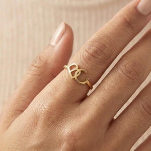 May include: A gold-toned ring featuring two interconnected capital letters, B and C, as the central focal point. The band is thin and circular, maintaining a consistent metallic finish throughout the design of the letters and the ring shank.
Custom Cursive Initial Ring, 14K Solid Gold, Romantic Script Jewelry