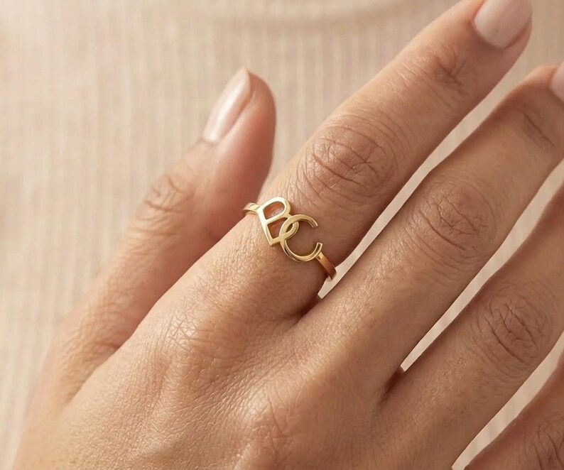 May include: A gold-toned ring featuring two interconnected capital letters, B and C, as the central focal point. The band is thin and circular, maintaining a consistent metallic finish throughout the design of the letters and the ring shank.
Custom Cursive Initial Ring, 14K Solid Gold, Romantic Script Jewelry