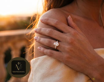 May include: A silver-toned ring featuring a large oval-cut center stone flanked by two smaller pear-cut stones on each side. The band is thin and metallic. A circular logo in the corner displays the text ValorVeinJewelry with a diamond icon.