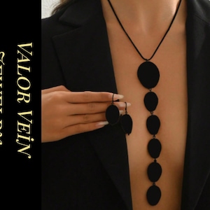 Puede incluir: Collar negro y pendientes a juego con una serie de colgantes circulares conectados. La joyería se muestra sobre un fondo oscuro, con el texto "VALOR VEIN JEWELRY" en letras doradas.