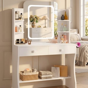 May include: A white vanity table featuring a rectangular mirror with an integrated LED light frame. The unit includes two drawers, side shelving units for storage, and a lower open shelf holding a woven basket, folded linens, and two gift bags.