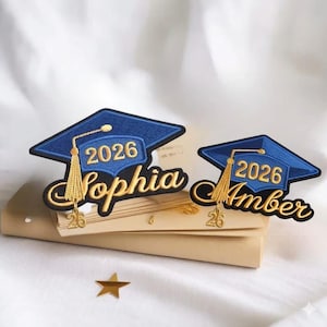 May include: Two graduation cap patches. The caps are blue with gold tassels and the year "2026". One patch says "Sophia" and the other says "Amber". A gold star is in the bottom left corner.