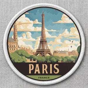 May include: Round patch featuring a stylized illustration of the Eiffel Tower in Paris, France, under a blue sky with clouds. The patch has a white border and the word "PARIS" in a dark green font.