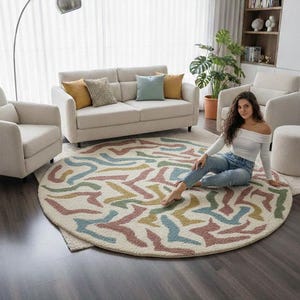 May include: A round area rug with a cream background and colorful abstract patterns in blue, green, yellow, and pink. The rug is in a living room setting with a sofa, chairs, and a floor lamp.