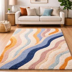 May include: A colorful area rug with a wavy pattern in shades of blue, orange, pink, and cream. The rug is placed on a hardwood floor in a living room setting, with a sofa and decorative pillows in the background.